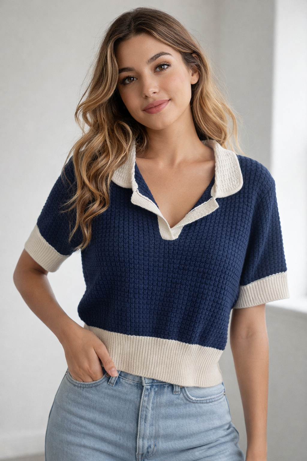 Woman wearing navy and cream textured knit collared top with short sleeves styled with light wash denim jeans